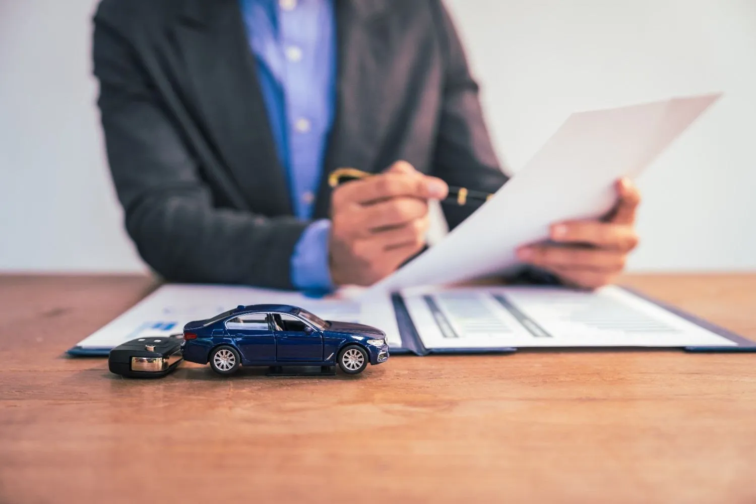 Person signing auto policy papers next to a toy car and keys