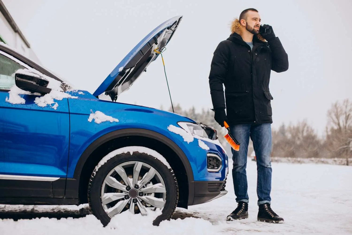 Driver beside a blue car with its hood up in the snow